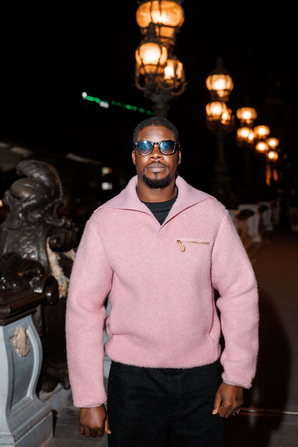 Portrait of a man in pink fleece half-zip, sunglasses, black trousers, bridge over the Seine, Paris at night