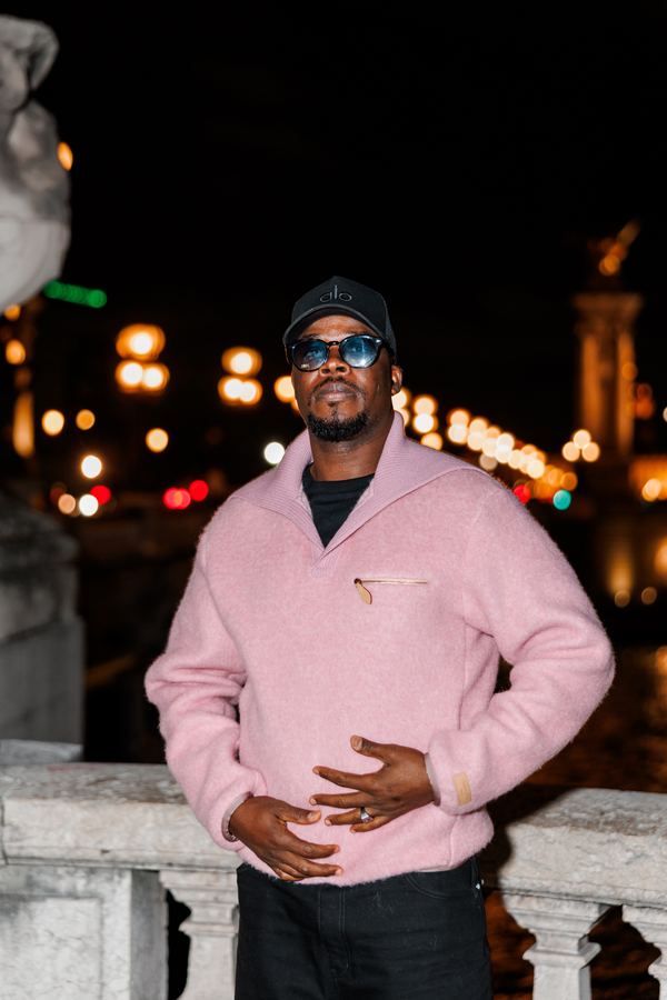 Portrait of a man in pink sweater, black cap, sunglasses, bridge over the Seine, Paris at night