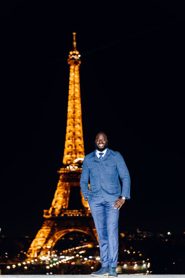 Portrait of a man in blue denim suit, tie, dark suede shoes, Eiffel Tower, Paris at night