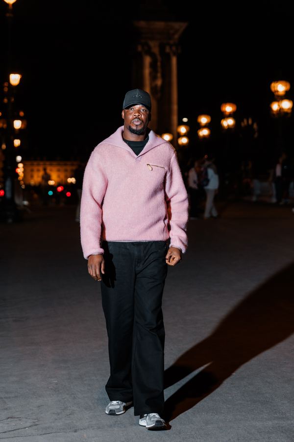 Portrait of a man in pink fleece half-zip, black cap, black trousers, bridge over the Seine, Paris at night