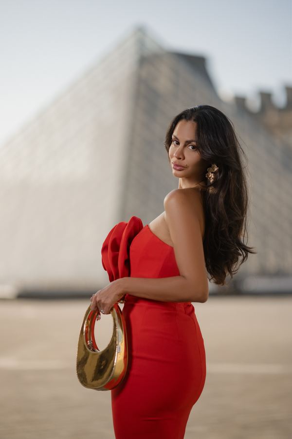 Portrait of a woman in red strapless midi dress, gold handbag, Louvre pyramid, Paris