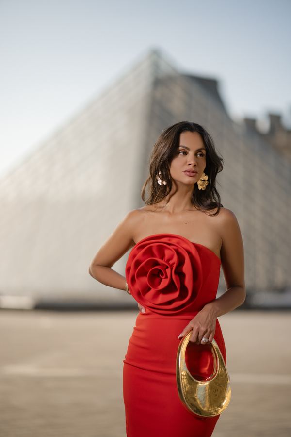 Portrait of a woman in red strapless midi dress, gold handbag, Louvre pyramid, Paris