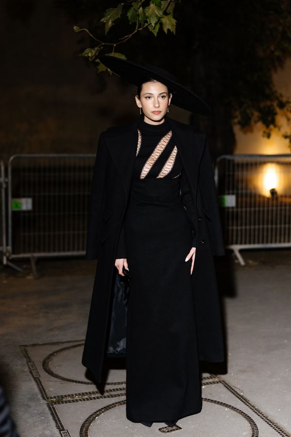 Street style at Paris Fashion Week: black long coat, black gown, wide-brim hat, show venue entrance, Paris at night