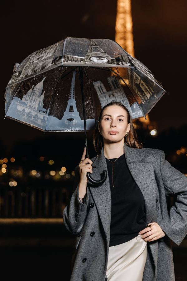 Portrait of a woman in grey long coat, black top, Eiffel Tower, Paris at night