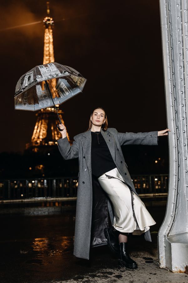 Portrait of a woman in grey long coat, beige slip skirt, black boots, Eiffel Tower, Paris at night