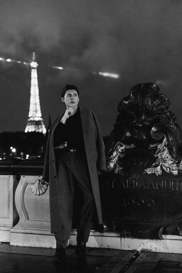 Portrait of a man in grey long coat, black top, Eiffel Tower, Paris at night
