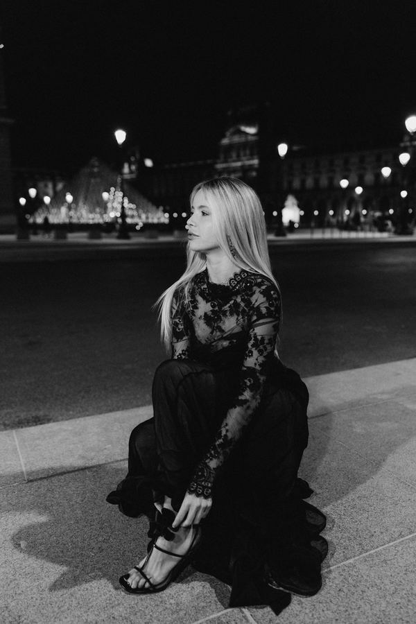 Portrait of a woman in black lace top, sheer black skirt, Louvre pyramid, Paris at night