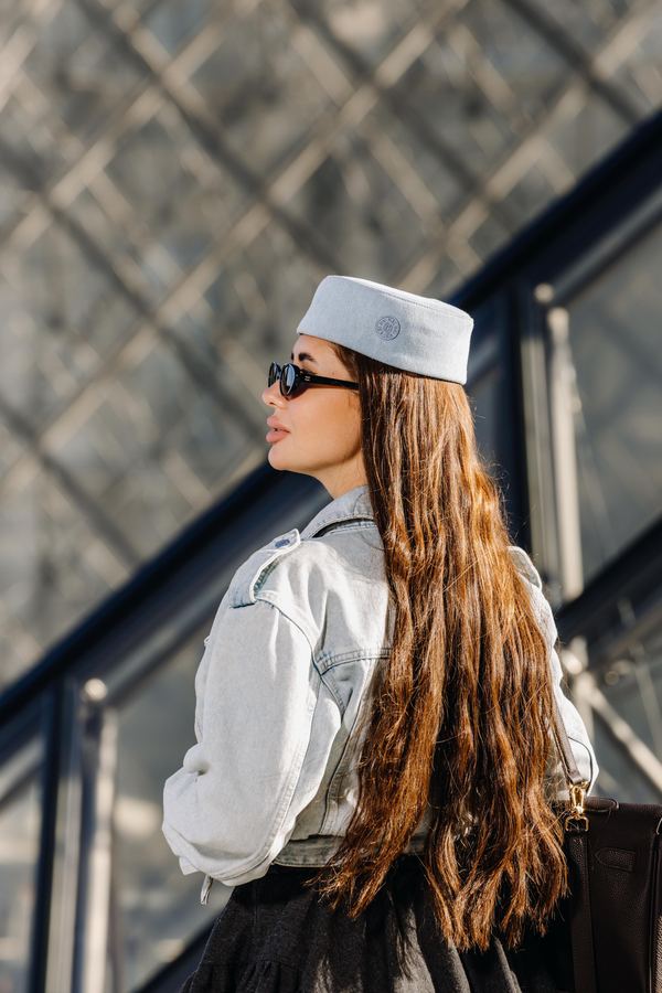 Portrait of a woman in grey denim jacket, sunglasses, white cap, Louvre pyramid, Paris